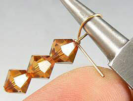 Bicone beads on a head pin being bent with pliers